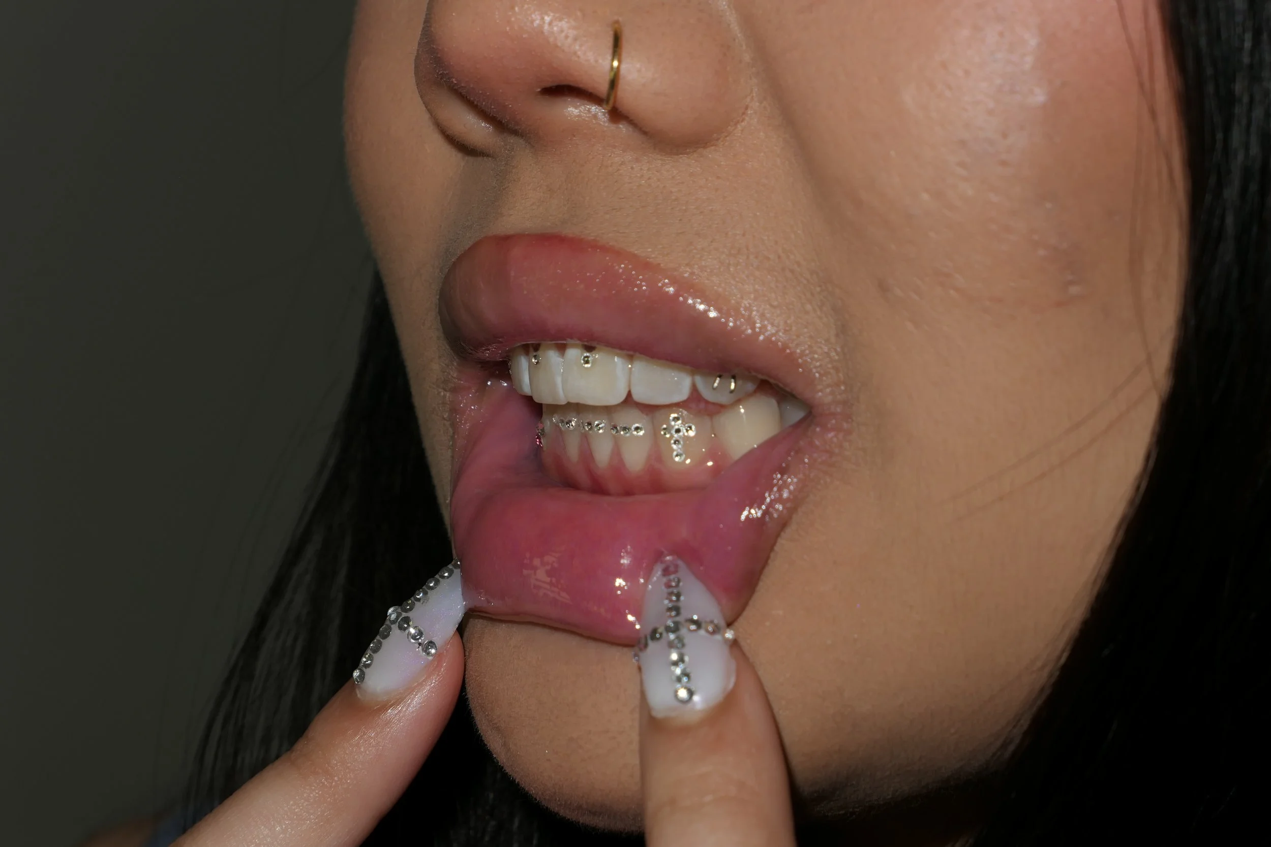 A single gem on a canine tooth, shown with metallic manicured nails at the lip.